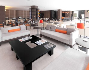 Un hall d’hôtel moderne doté d’un espace salon comprenant des canapés et des fauteuils, une table basse avec des magazines et une grande pièce décorative de forme cylindrique.