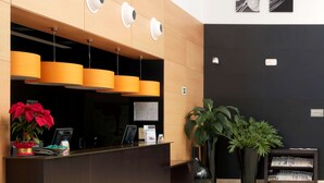 A modern reception area with a wooden panel wall, a dark reception desk, and a large potted plant. - NH Campo De Gibraltar (Los Barrios)