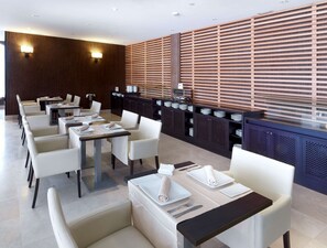 Eine moderne Hotelhalle mit einer langen Rezeption, mehreren Sitzbereichen mit Tischen und Stühlen sowie einer dekorativen Holzwand mit Schlitzmuster.