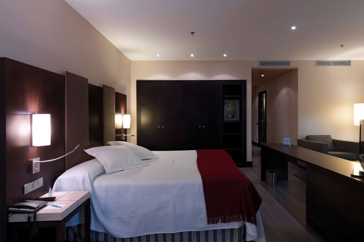 Une chambre d’hôtel avec un lit, une table de chevet, une lampe et une armoire sombre.