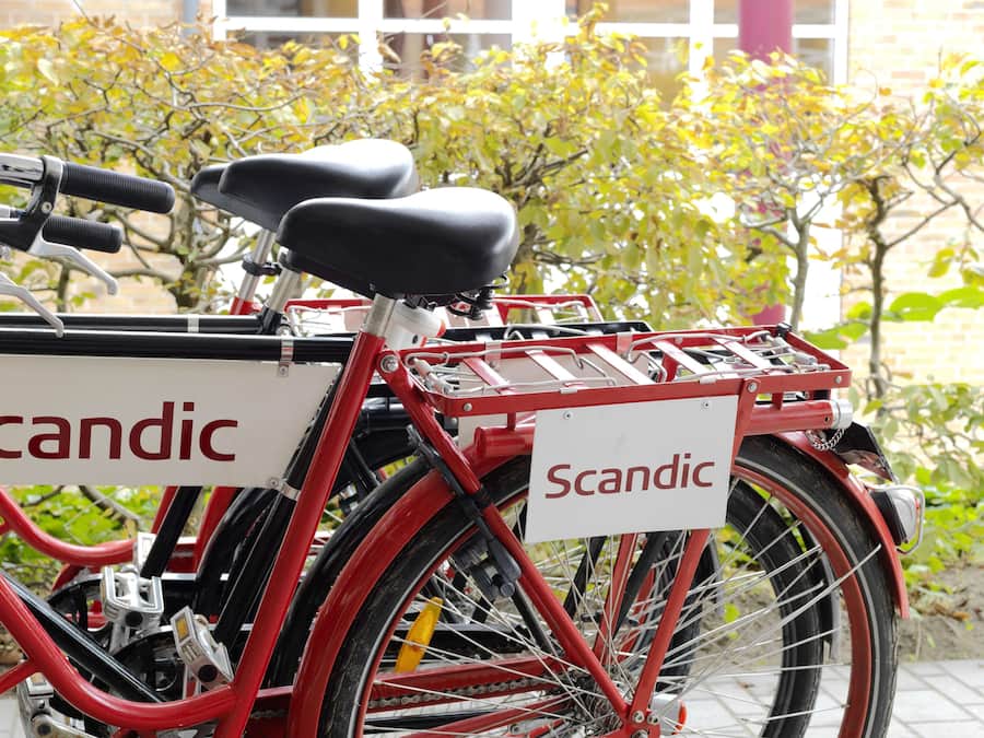 A red bicycle with a basket and a sign that reads "Scandic."