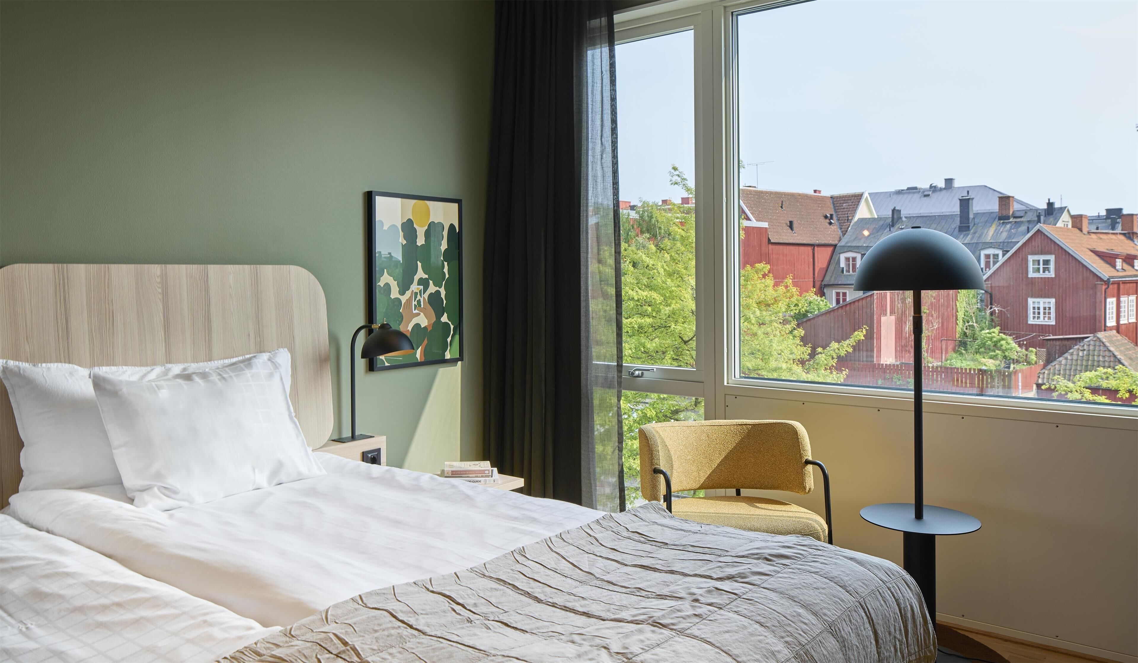 A bedroom with a large bed, a chair, a desk, and a window with a view of buildings.