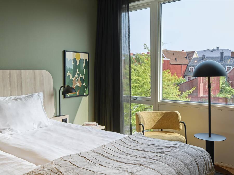 A bedroom with a large bed, a chair, a desk, and a window with a view of buildings.