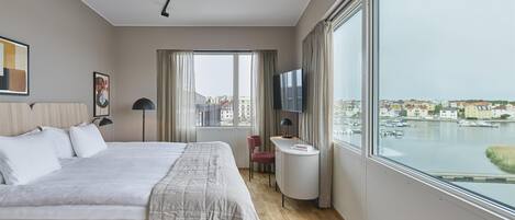 Habitación de hotel moderna con una cama grande, un escritorio, un televisor y vistas al puerto.