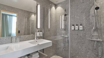 A modern bathroom with a large white sink, a glass shower enclosure, and a mirror with vertical light fixtures.