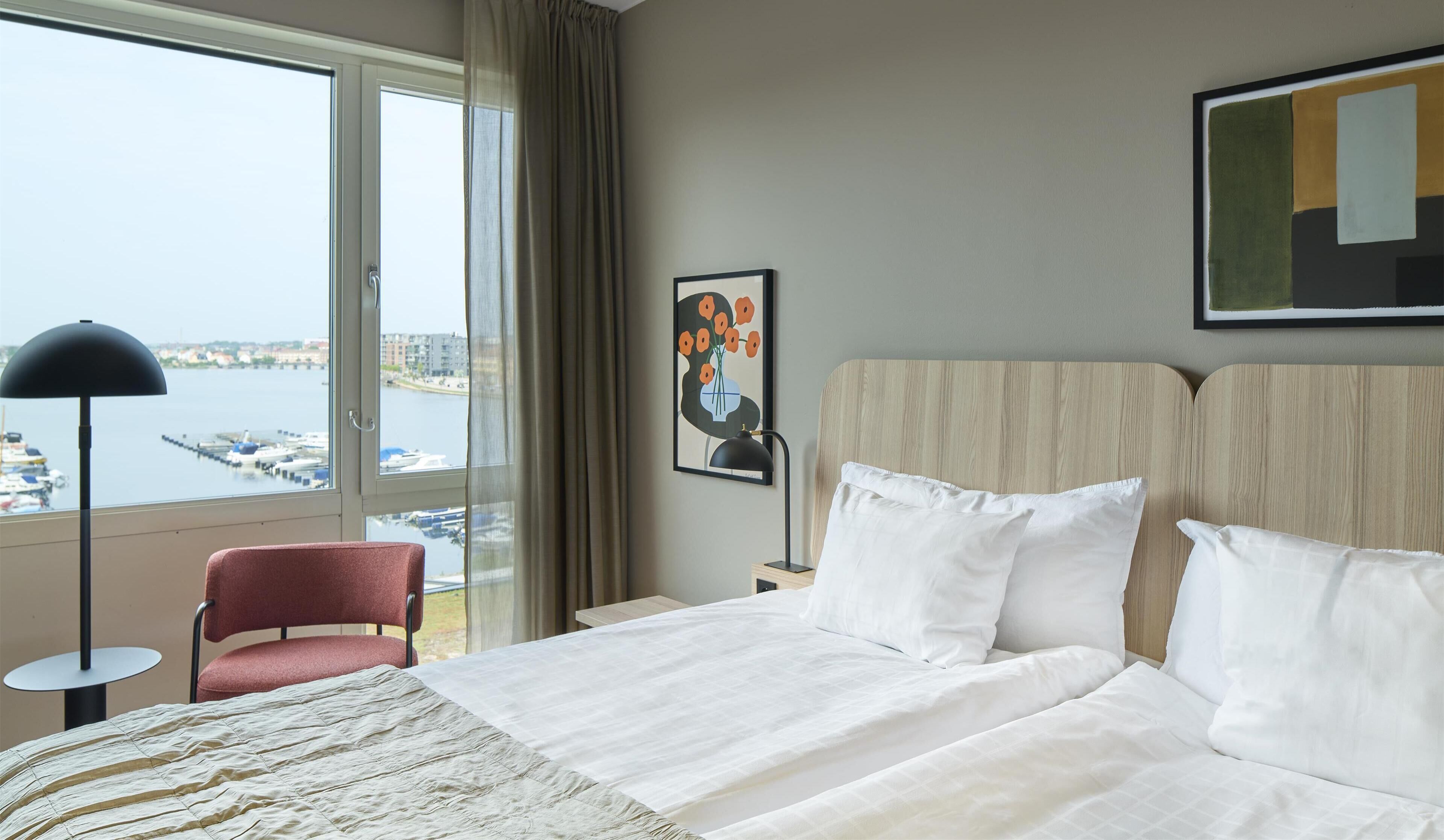 Habitación de hotel con cama, una silla, una lámpara y vistas al puerto deportivo.