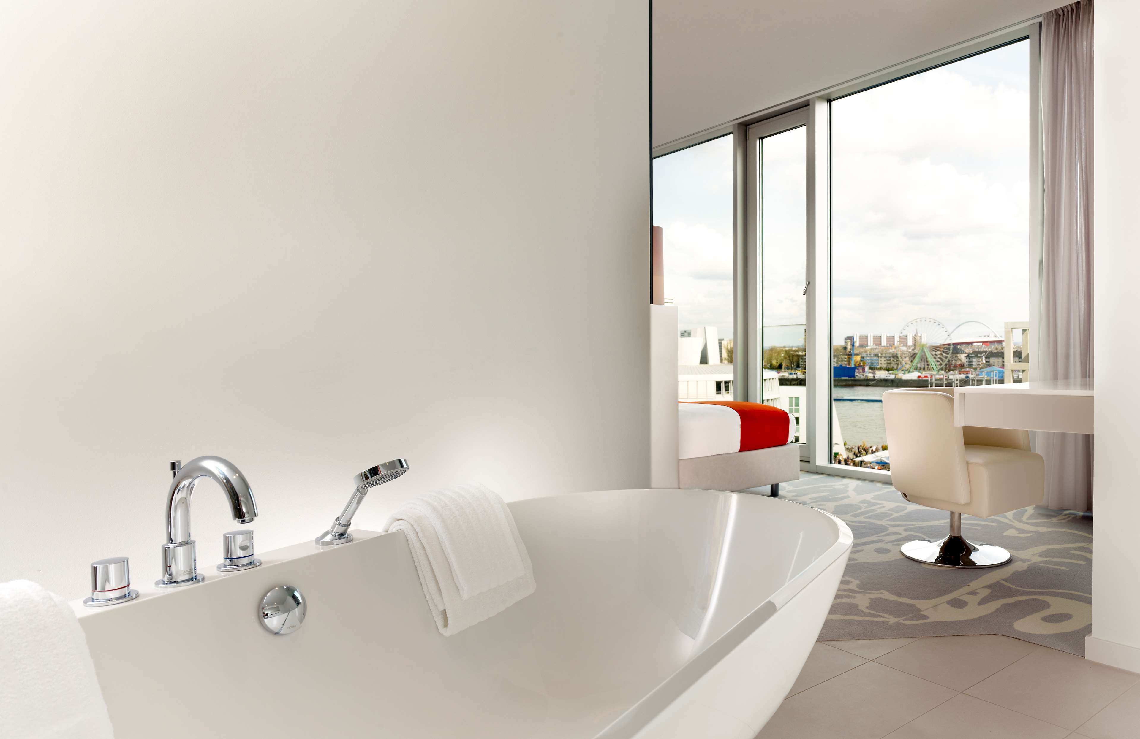 Un baño moderno con una bañera grande, ducha y retrete. Una ventana amplia ofrece vistas a un paisaje urbano y una noria.