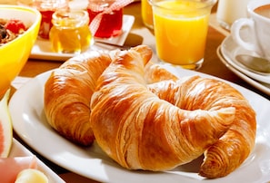 En frukostuppläggning med croissanter, apelsinjuice och en skål med flingor.
