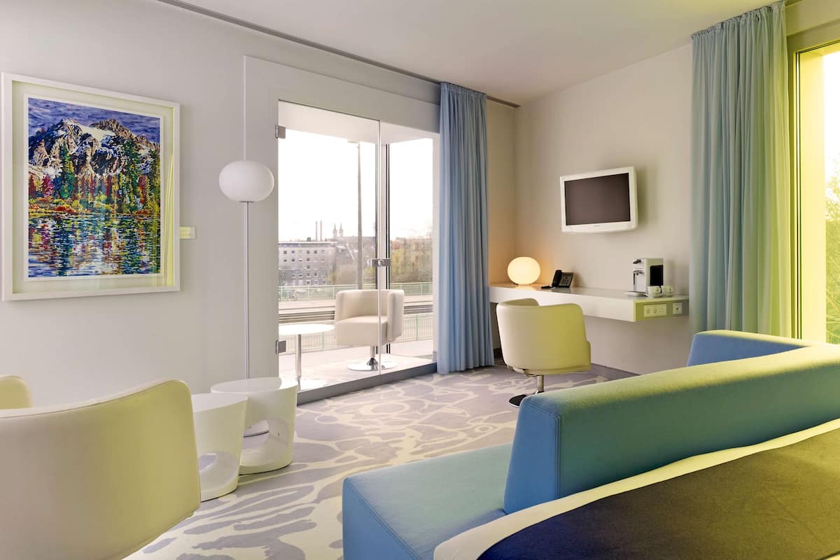 Ett hotellrum med en säng, ett skrivbord, en stol, en tv och en tavla.