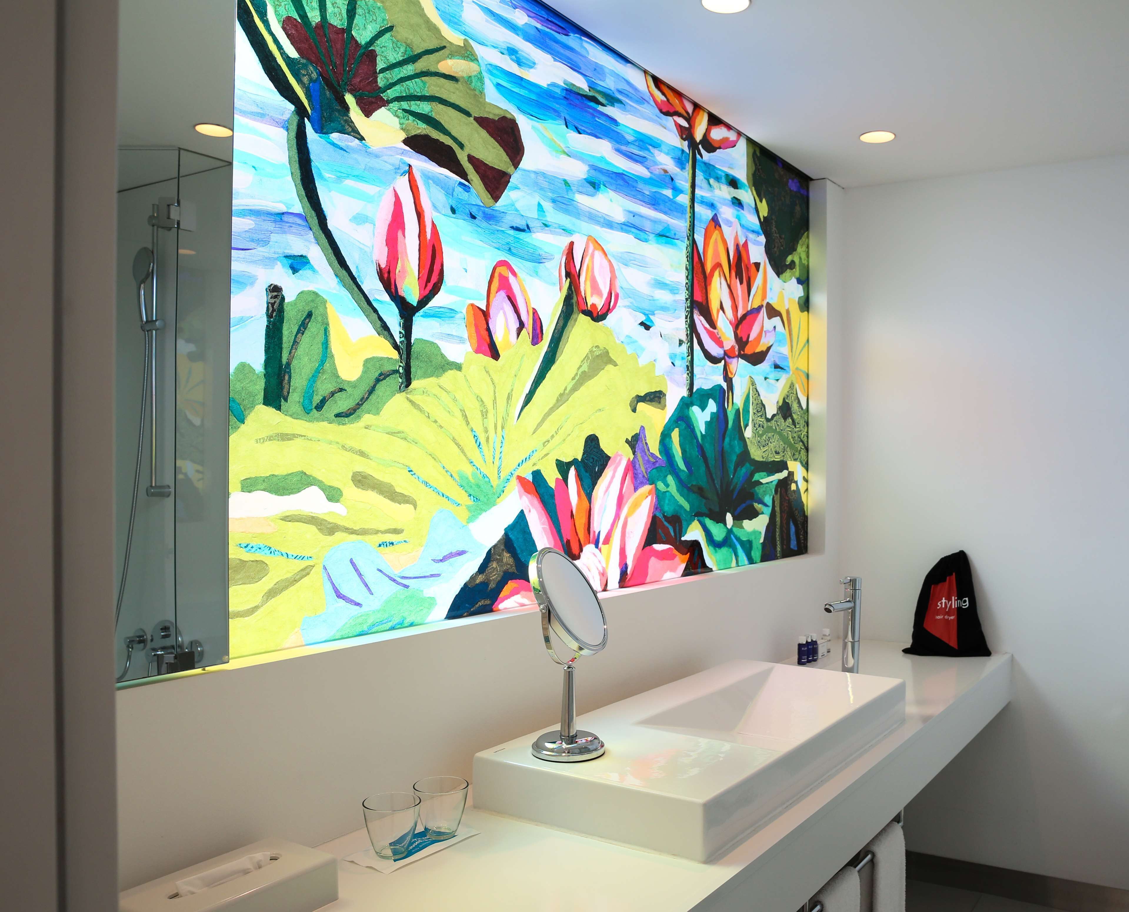 A bathroom with a large mirror, a white sink, and a colorful floral mural on the wall.