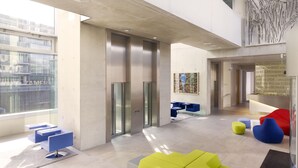 A modern lobby with a high ceiling, large windows, and a mix of seating areas including colorful sofas and chairs. - art'otel Cologne (Cologne)