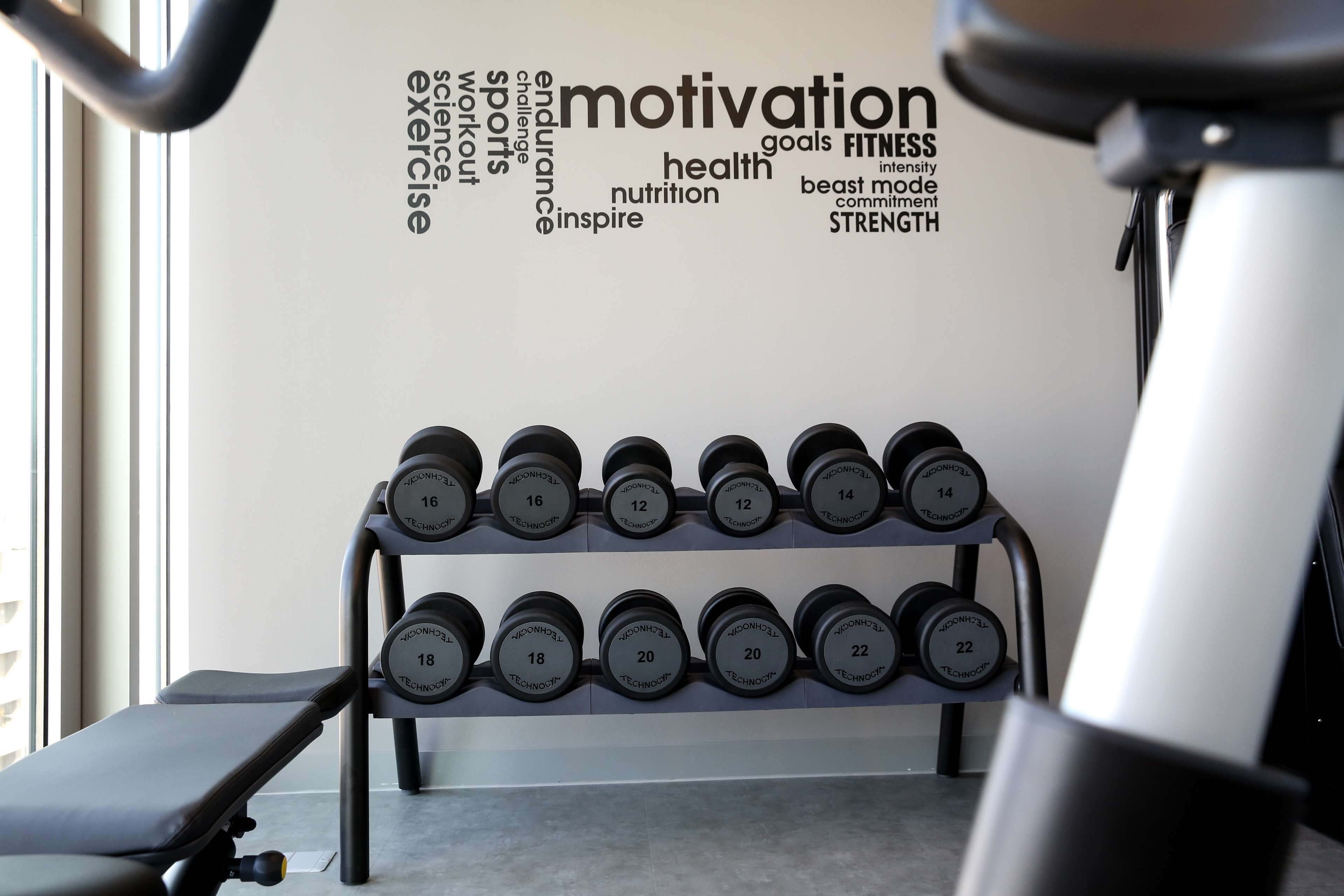 A gym with a wall of motivational words and a rack of dumbbells.