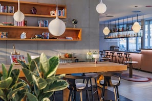 A bar area with wooden shelves, hanging pendant lights, and a bar counter with stools. - art'otel Cologne (Cologne)