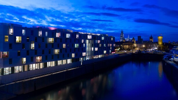 A modern building with multiple windows and a bridge over a river. - art'otel Cologne (Cologne)