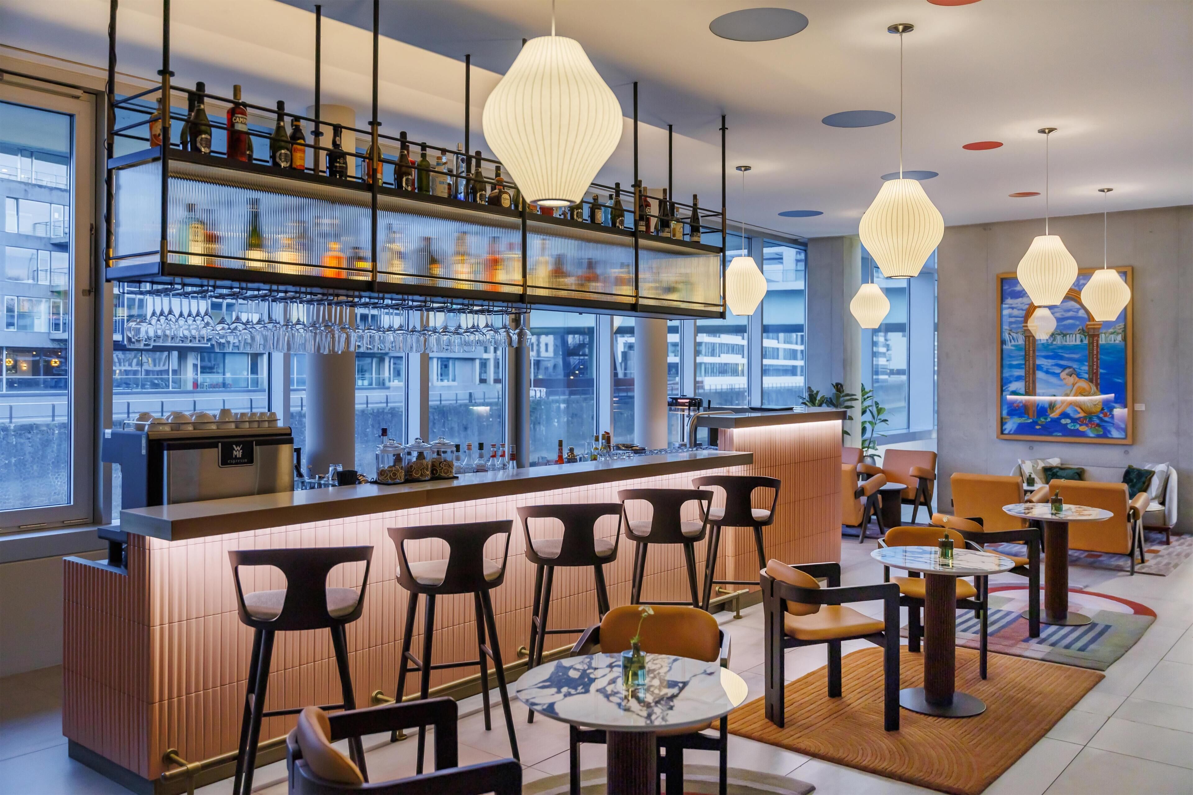 A modern bar area with a glass display case, bar stools, and hanging pendant lights.