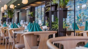 A restaurant with wooden chairs, tables with green napkins, and potted plants. - art'otel Cologne (Cologne)