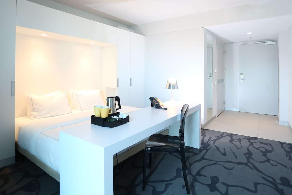 Ett hotellrum med en säng, ett skrivbord, en stol, en lampa och en kaffebryggare.