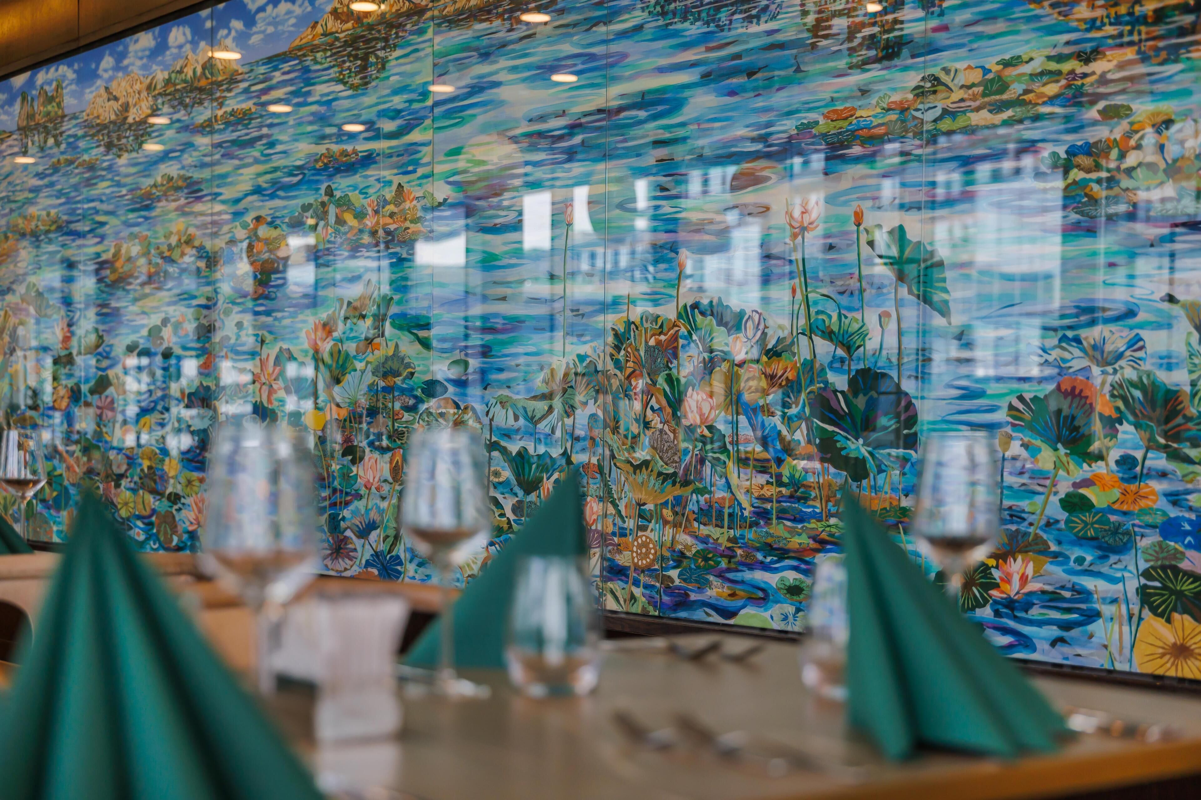 Un ristorante con un vivace murale floreale sulla parete, una zona bar con bicchieri e tovaglioli, e un' disposizione di tavoli.