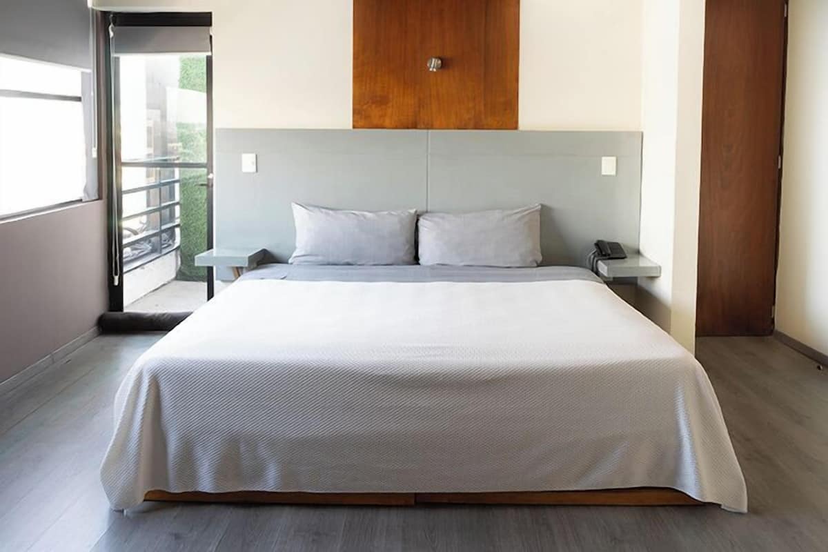 Un dormitorio moderno con una cama grande, dos mesitas de noche, un cabecero de madera y un ventanal corredero que da a un balcón.