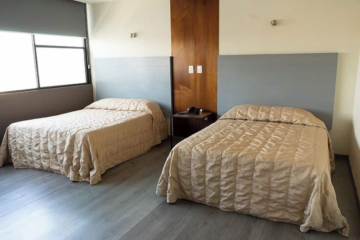 Dos camas individuales con ropa de cama color crema en una habitación con suelo de madera y una pared de acento de madera.