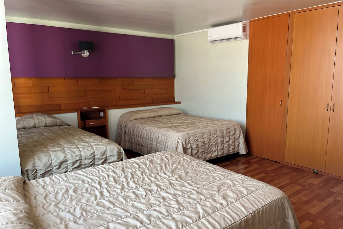 Habitación con dos camas, un armario de madera, una pared morada y un equipo de aire acondicionado.
