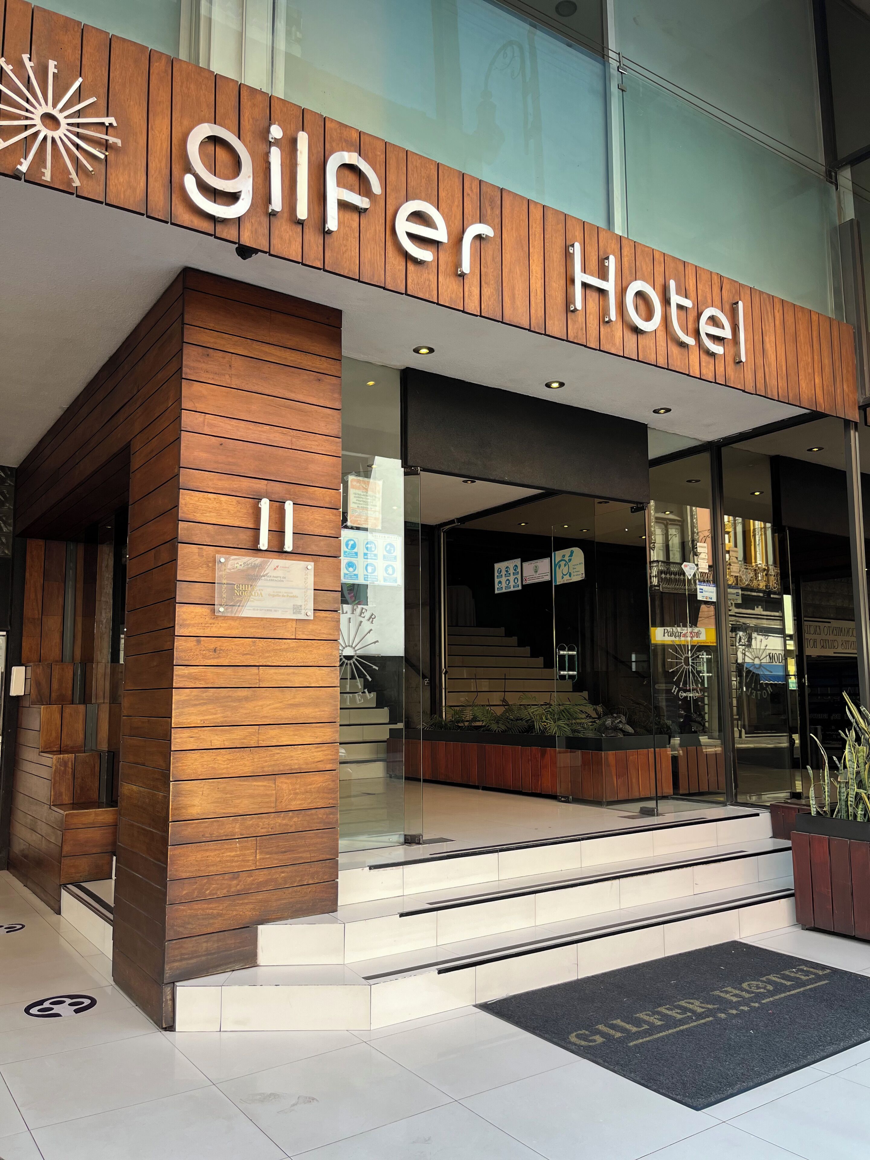 Exterior del Hotel Gilfer, con fachada de madera, entrada de vidrio y un cartel con el nombre del hotel.