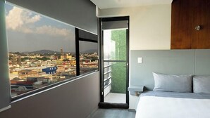 A modern hotel room with a large window offering a city view, a balcony with a green wall, and a neatly made bed. - Hotel Gilfer Puebla Centro Histórico (Puebla)