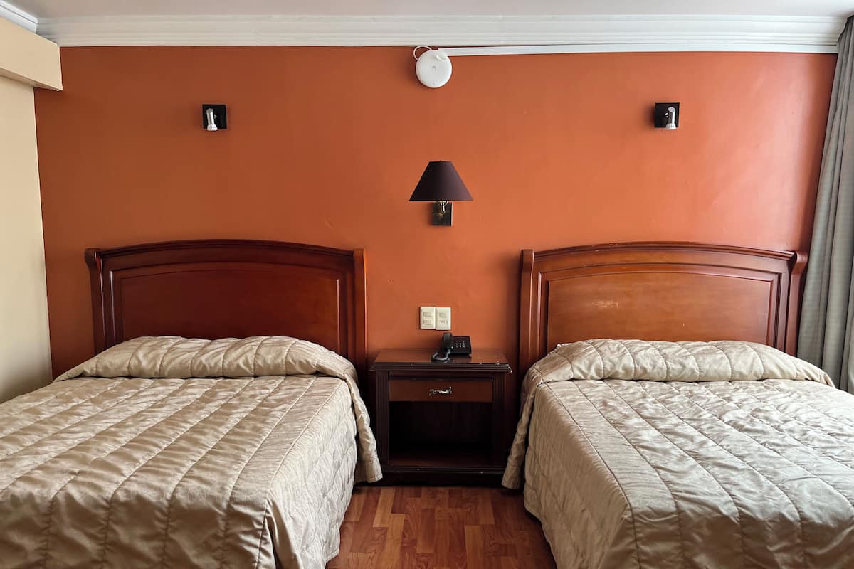 Habitación de hotel con dos camas, una mesita de noche con lámpara y teléfono en la pared.