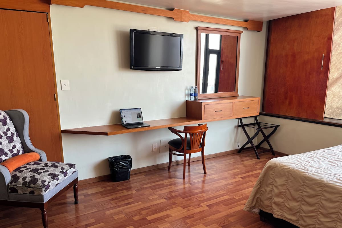 Un dormitorio con un escritorio de madera, una silla, una cama y un televisor en la pared.