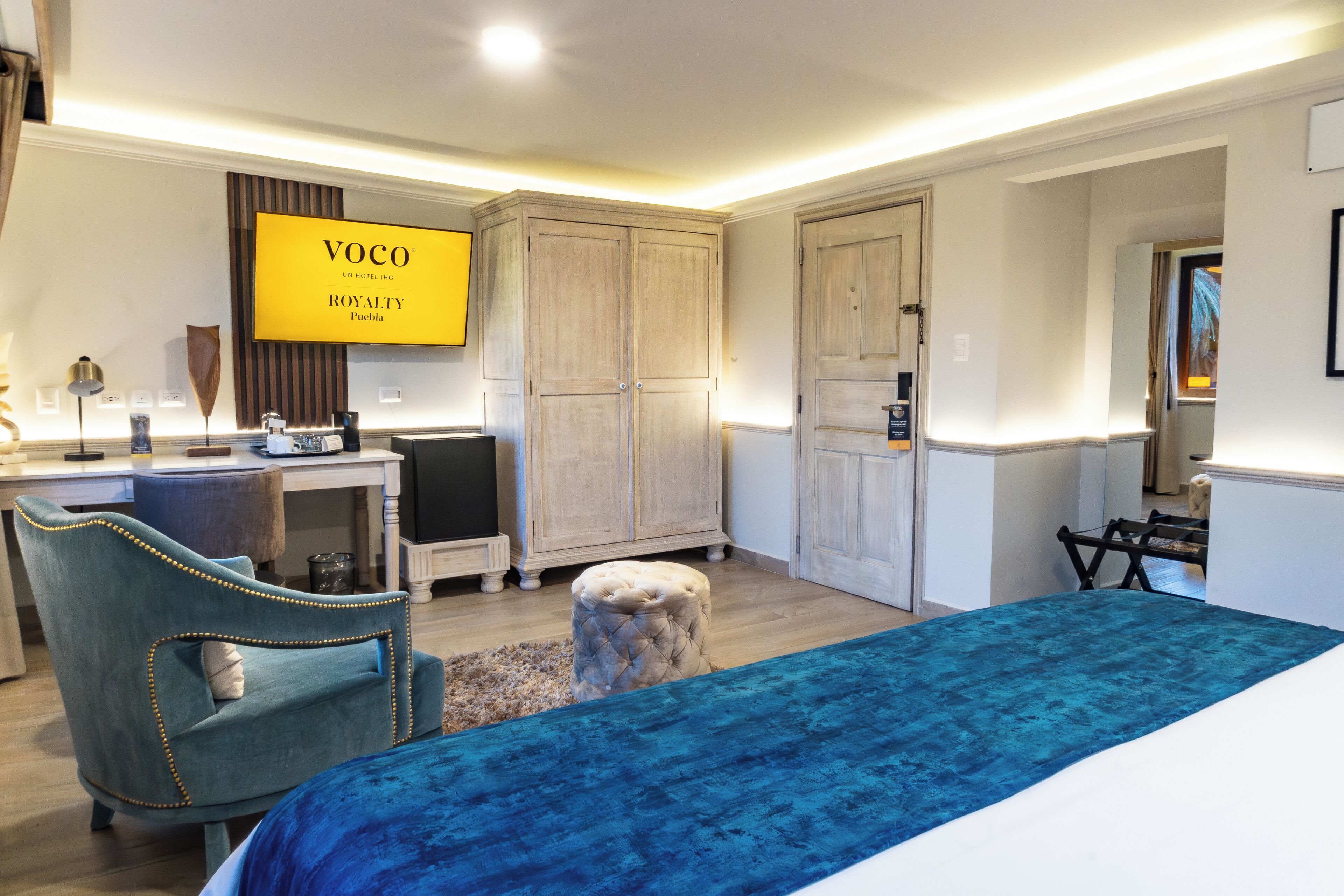 Une chambre d’hôtel équipée d’un lit, d’un bureau, d’une chaise, d’une armoire et d’un téléviseur affichant le nom de l’hôtel.