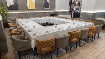 A conference room with a long table, chairs, and a bar area in the background.