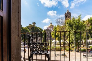 Un balcon doté d’une balustrade en fer forgé, d’un banc et offrant une vue sur un bâtiment historique avec un dôme et une tour.