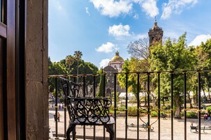 Un balcón con barandilla de hierro forjado, una banca y vistas a un edificio histórico con cúpula y torre.