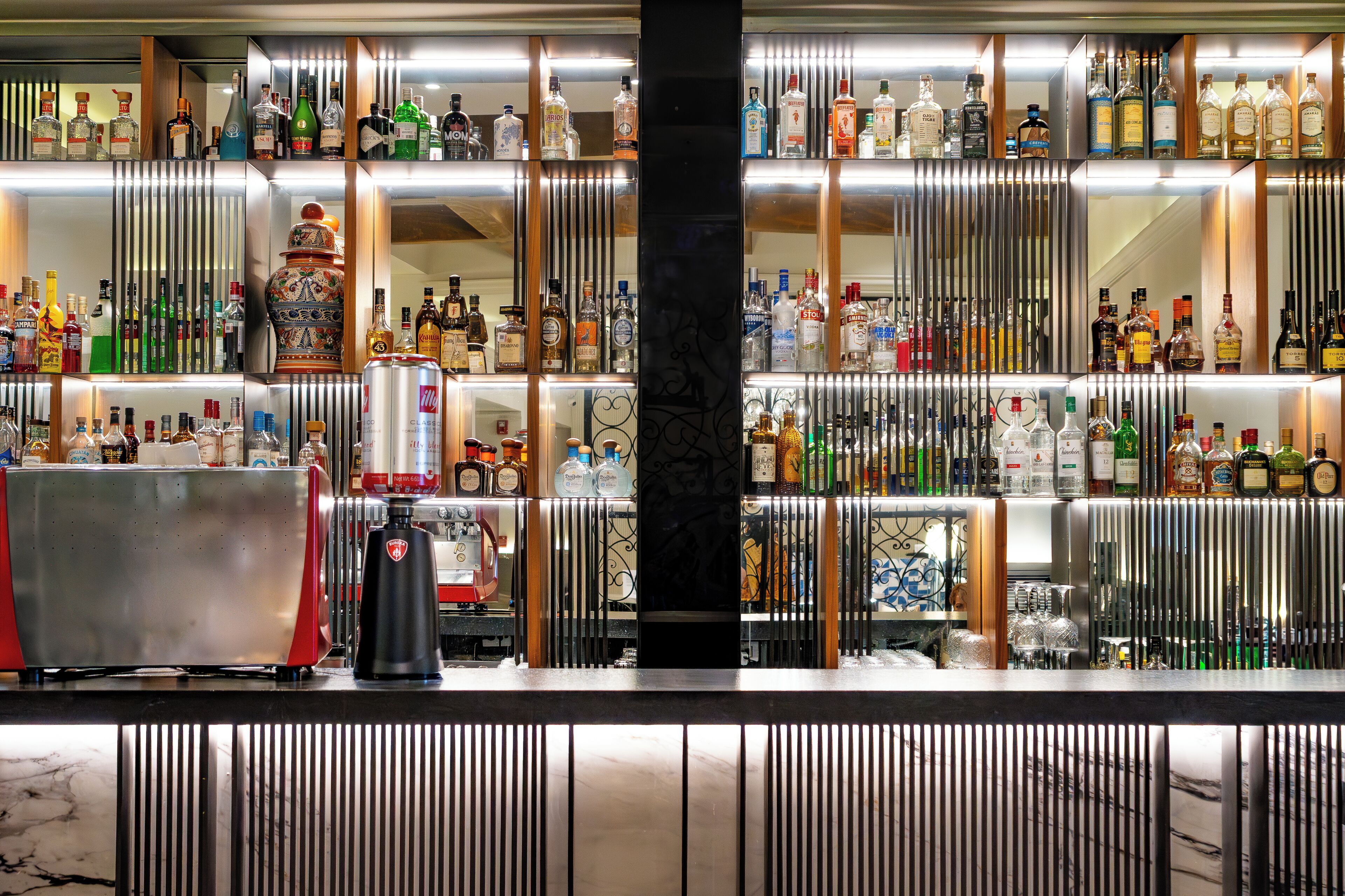 A bar area with shelves of various liquor bottles, a coffee machine, and a decorative vase.