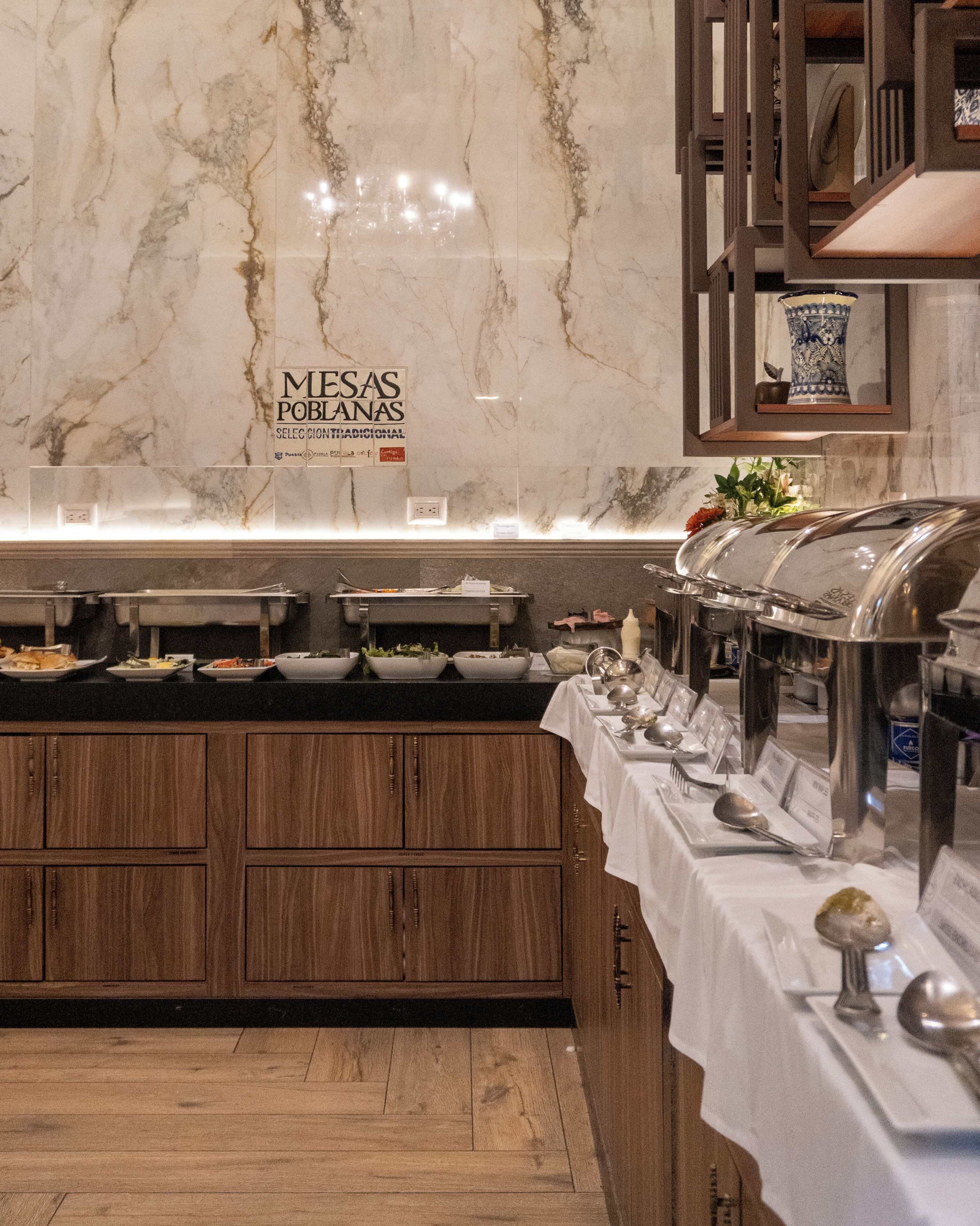 A buffet setup with multiple serving stations, a marble wall, and a sign indicating 'MESAS POBLANAS'.