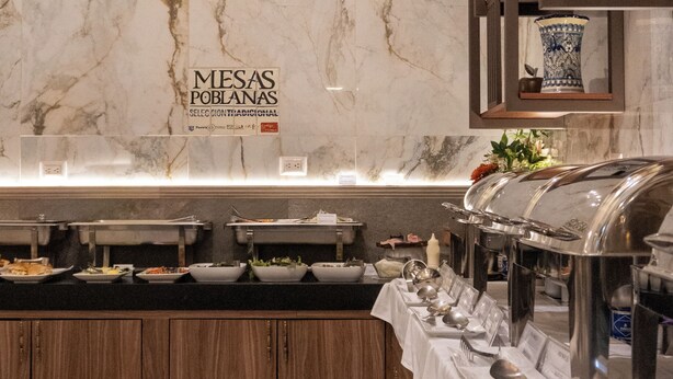 A buffet setup with multiple serving stations, a marble wall, and a sign indicating 'MESAS POBLANAS'. - voco Royalty Puebla Downtown by IHG (Puebla)