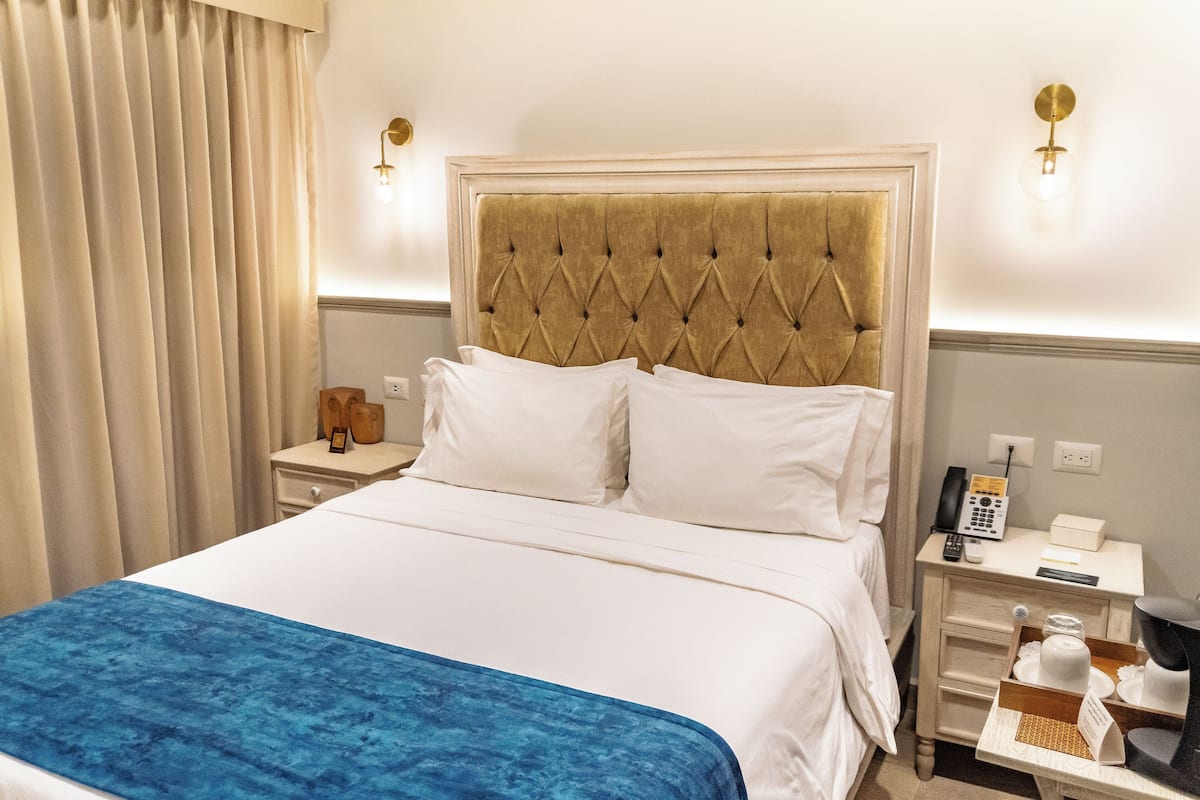 A hotel room with a large bed, a bedside table with a lamp, a telephone, and a small nightstand.