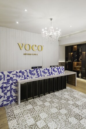 Un comptoir d’accueil au design moderne, avec un revêtement frontal en carreaux bleus et blancs formant un motif, et un lustre suspendu au-dessus.