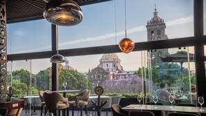 An outdoor dining area with tables and chairs, a view of a historic building, and hanging pendant lights. - voco Royalty Puebla Downtown by IHG (Puebla)