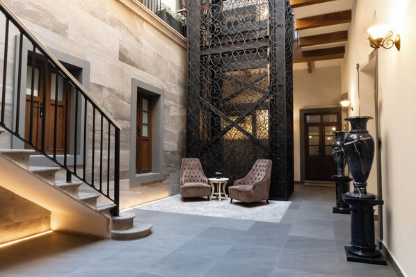 A spacious hallway with a staircase, two armchairs, a small table, and decorative vases.