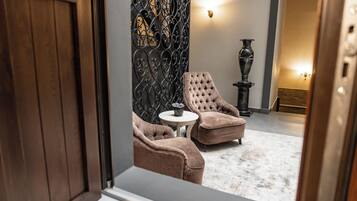 A room with a wooden door, a patterned wall, two armchairs, a small round table, and a vase.