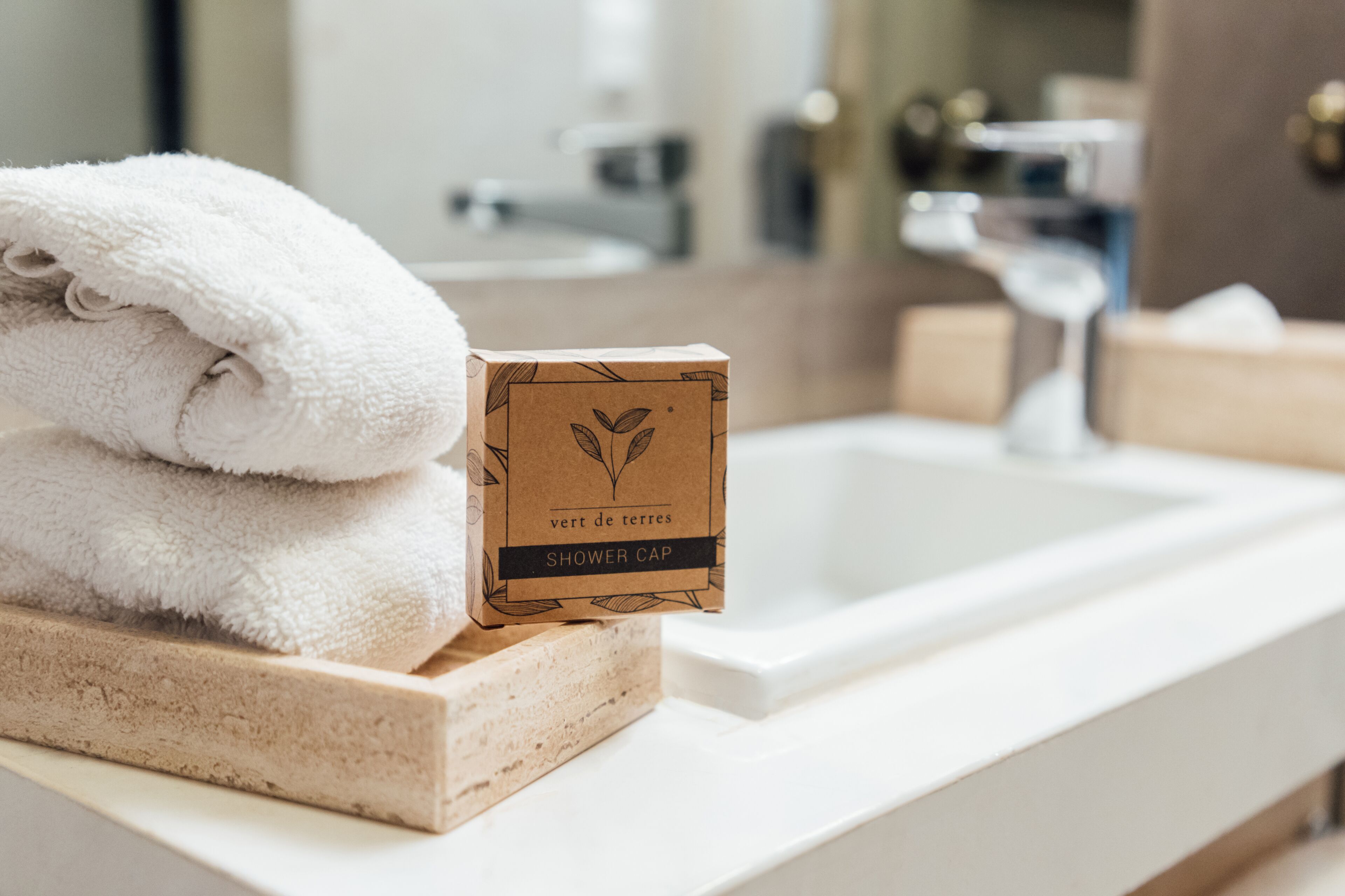A bathroom with a white sink, a towel, and a shower cap on a wooden tray.
