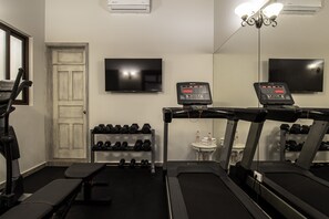Une salle de sport équipée de tapis de course, d’haltères et d’un téléviseur fixé au mur.