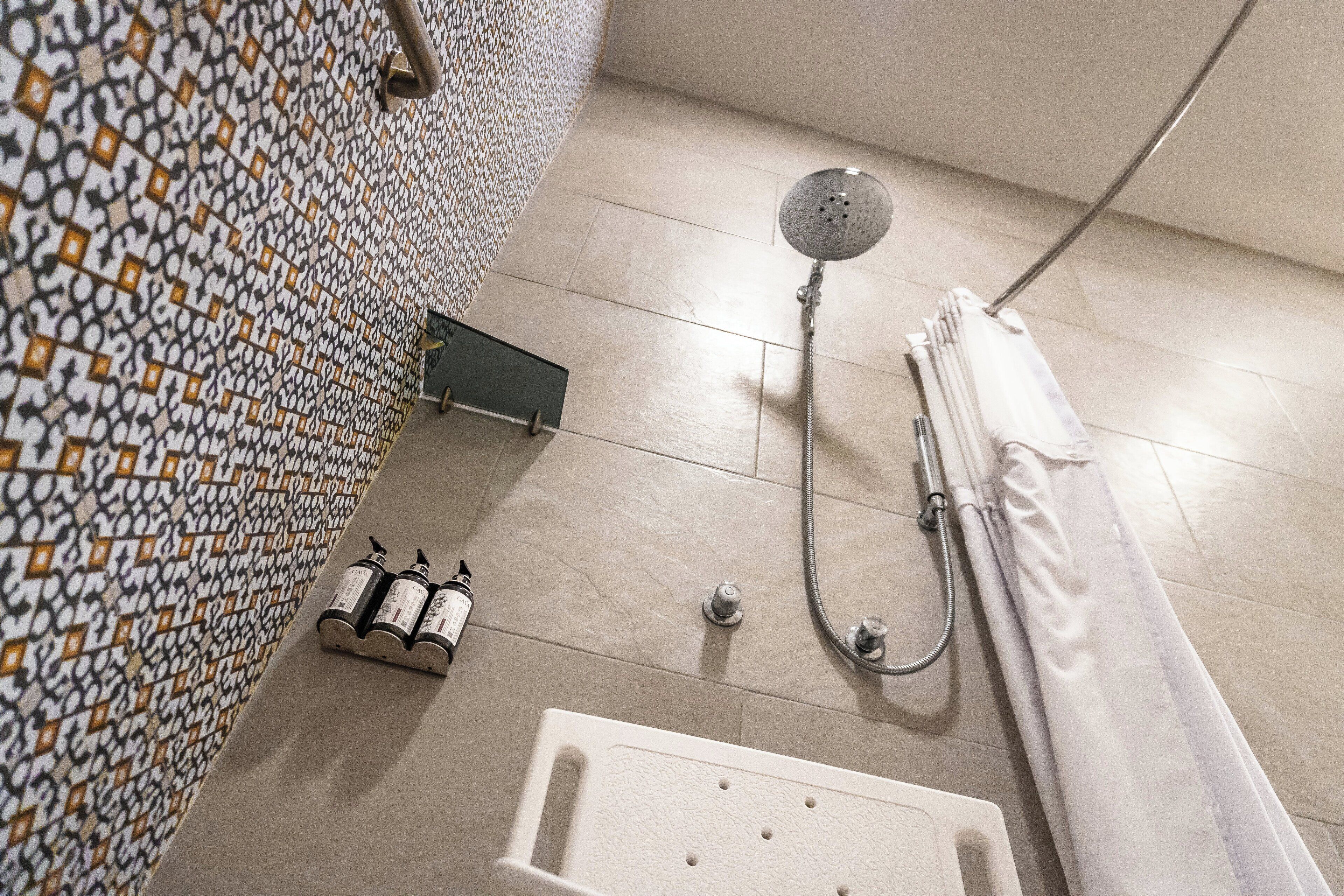 A bathroom with a patterned wall, a showerhead, a bathtub, and two bottles of shampoo.