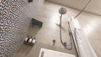 A bathroom with a patterned wall, a showerhead, a bathtub, and two bottles of shampoo.