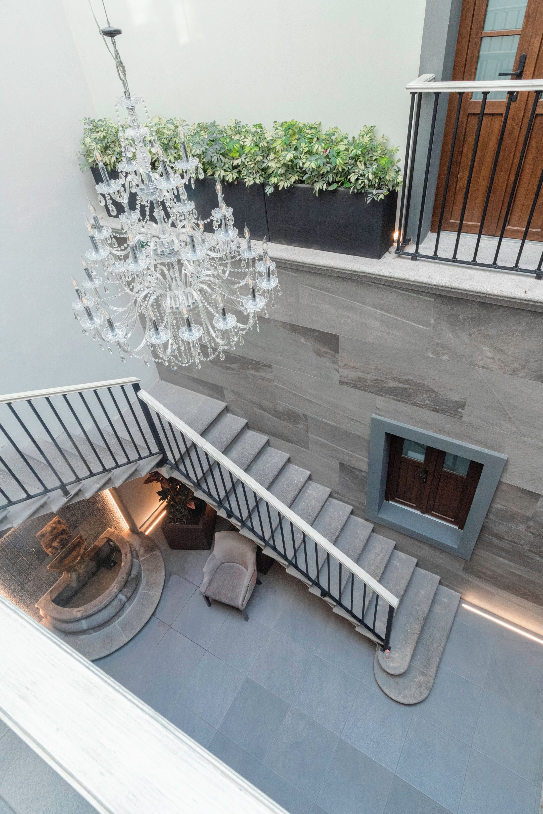 A staircase with a chandelier, a small seating area, and a window with a view of greenery.