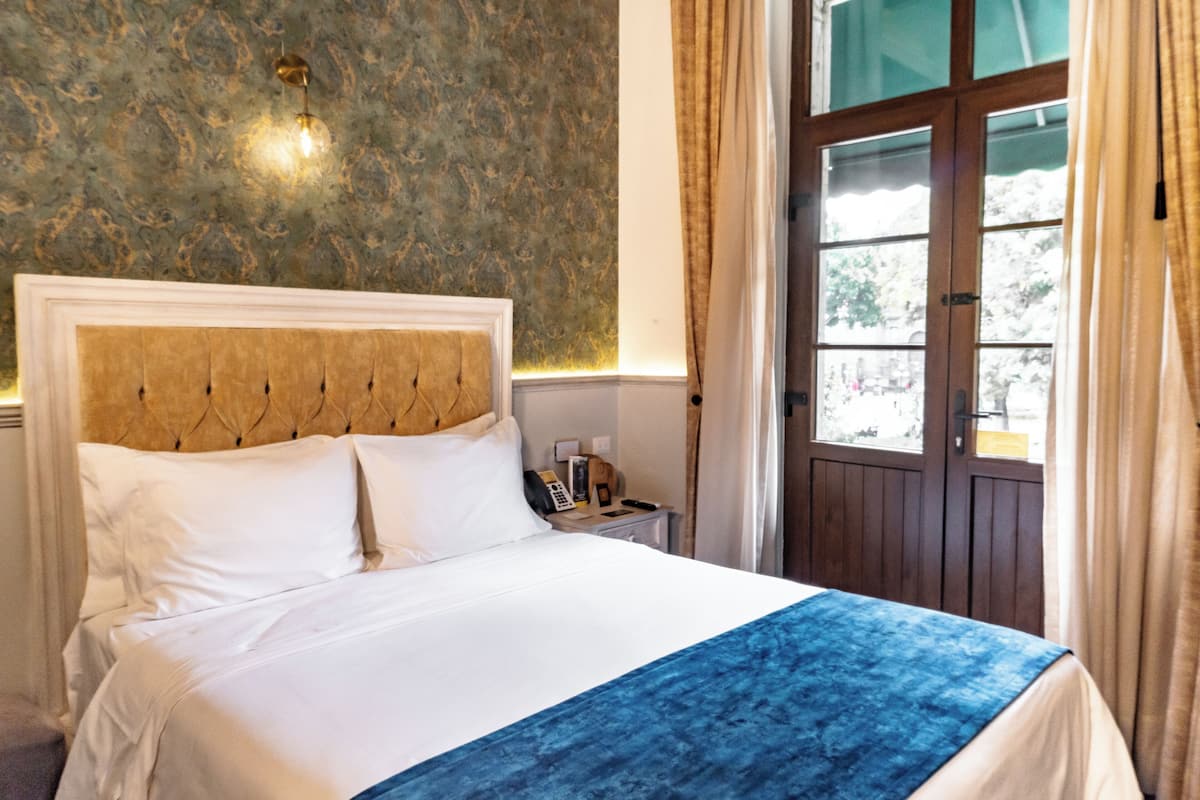 A hotel room with a large bed, a wooden headboard, a telephone, and a window with curtains.
