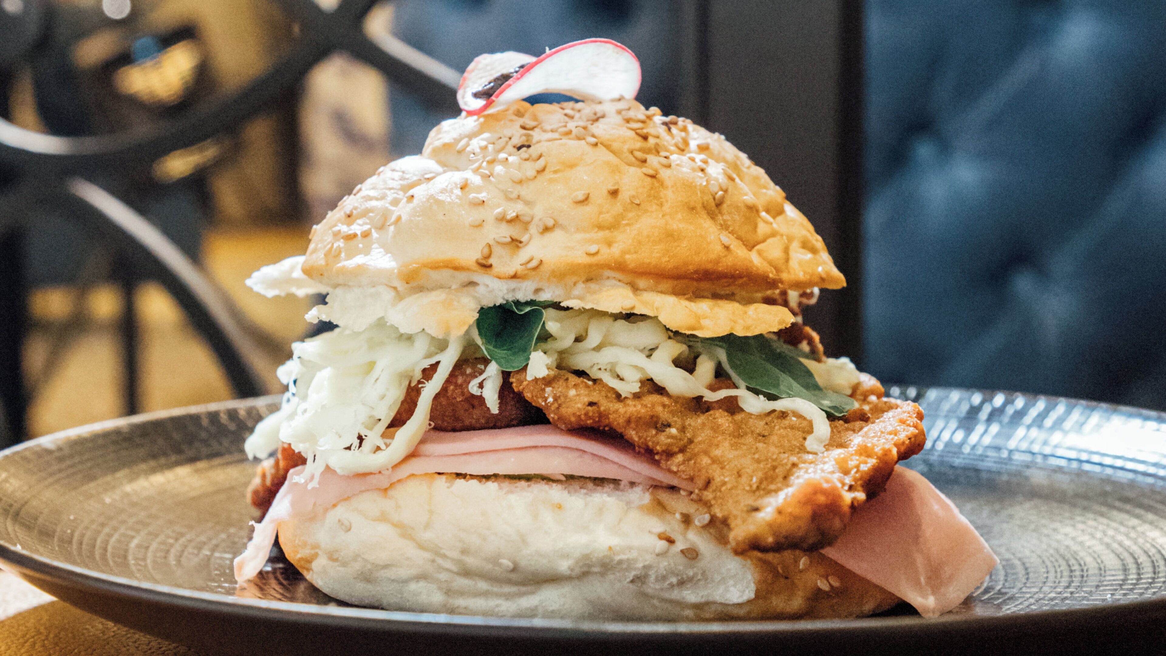 A sandwich with a sesame seed bun, lettuce, and a fried patty, served on a plate.