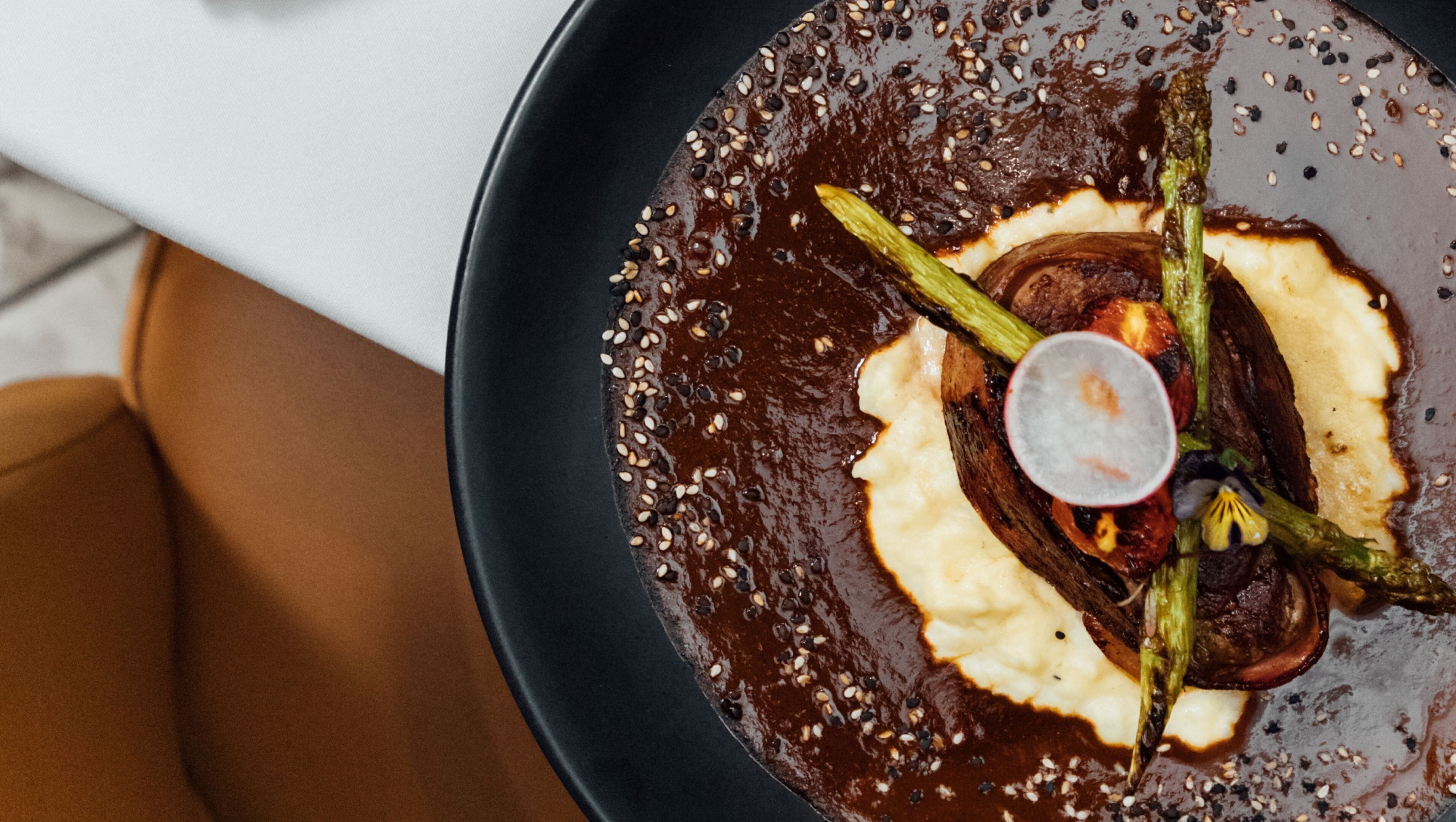 Un plato con salsa oscura, una cucharada de crema y espárragos.