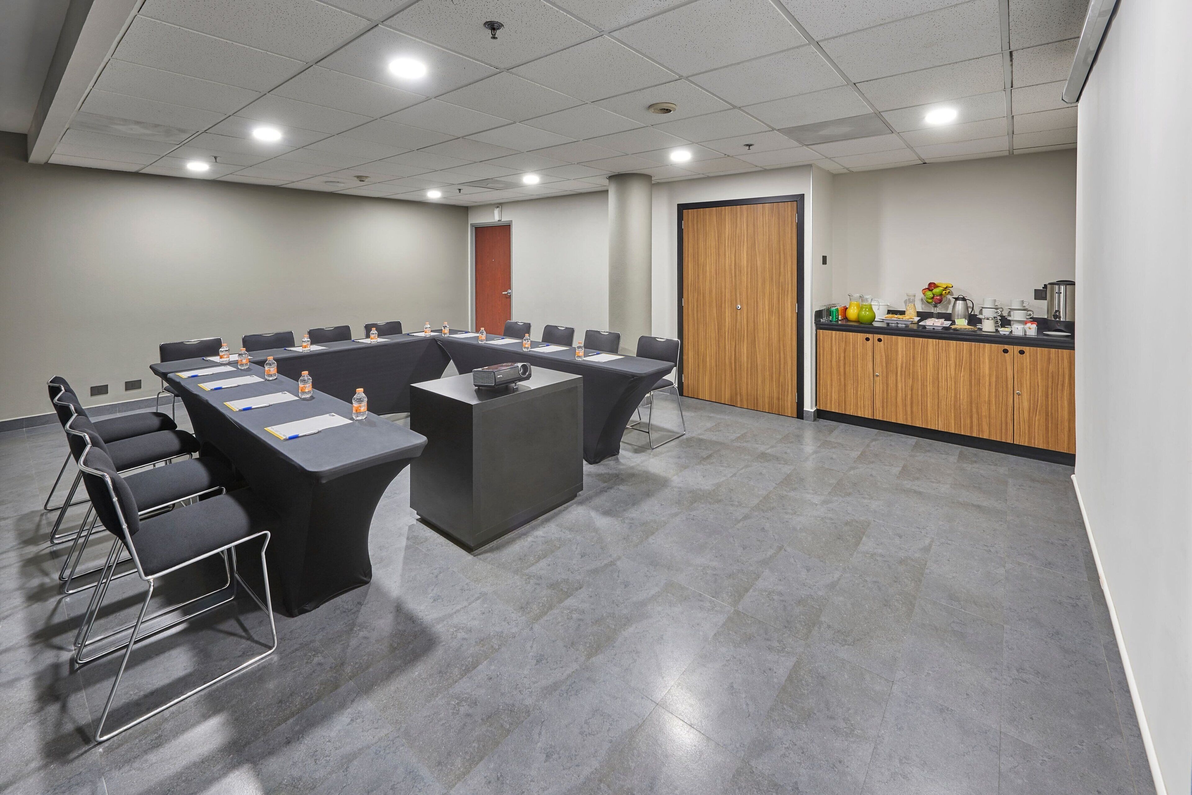 A conference room with a long table, chairs, a podium, and a kitchenette area.